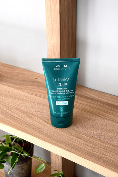 Aveda Botanical Repair Masque Light-tube på en trehylle mot grå vegg, med en grønn plante