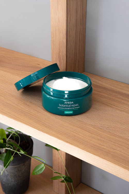 Åpen krukke med Aveda Botanical Repair Masque Rich på en trehylle, med kremen synlig